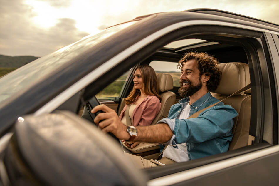 A guy driving while a woman is sitting in the passenger seat. Both smiling and enjoying their ride.